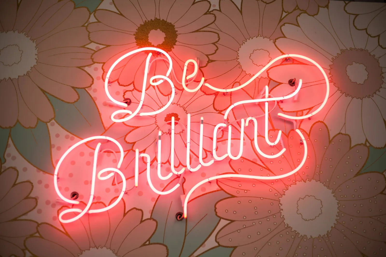 Be Brilliant neon sign against vintage floral wallpaper